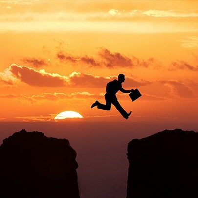 a man jumping from one cliff to another with sun in the background